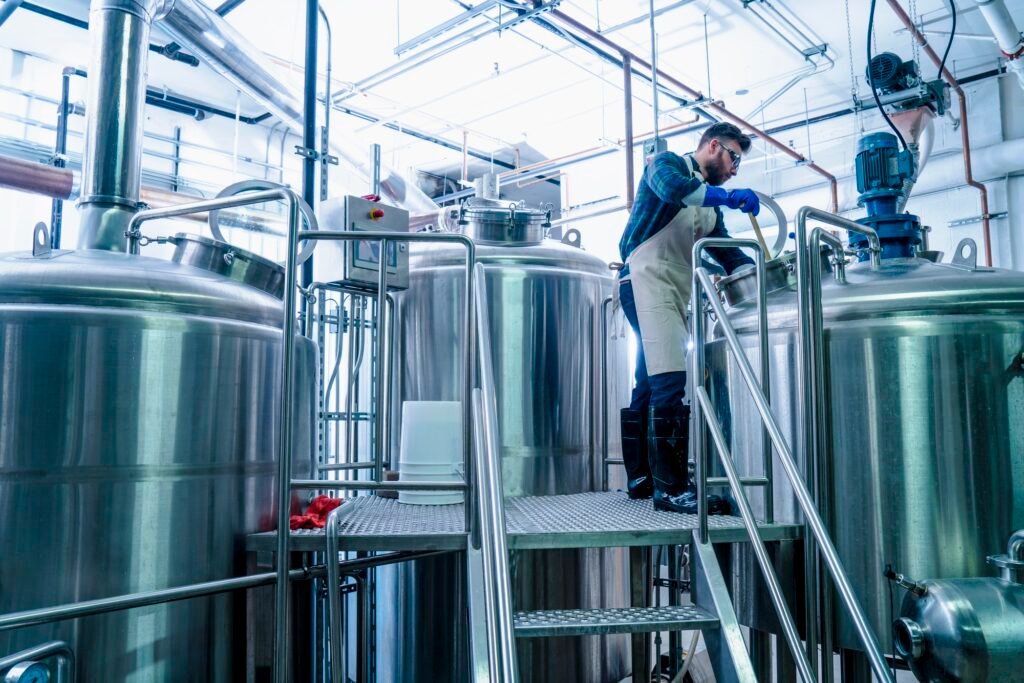 Young man in brewery wearing apron testing beer in tank